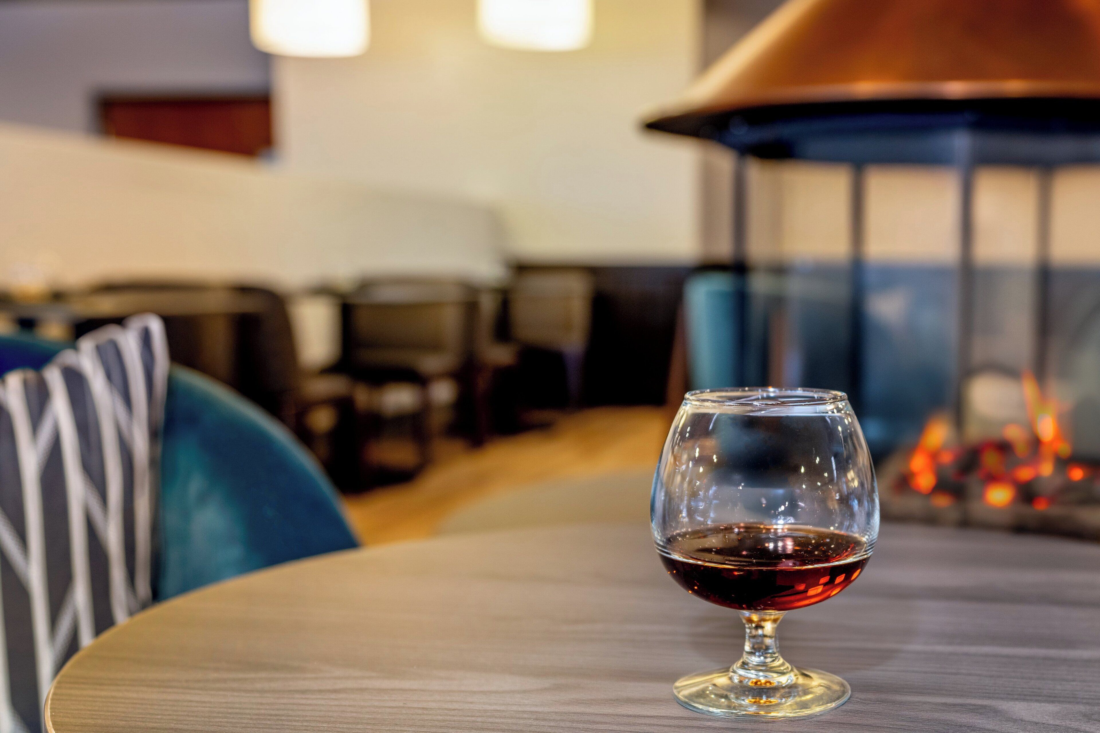 Una copa de vino tinto sobre una mesa en un restaurante con una decoración moderna y una chimenea al fondo.