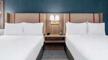 Une chambre d’hôtel avec deux lits, une tête de lit en bois, des tables de chevet avec des lampes et un tapis à motifs.