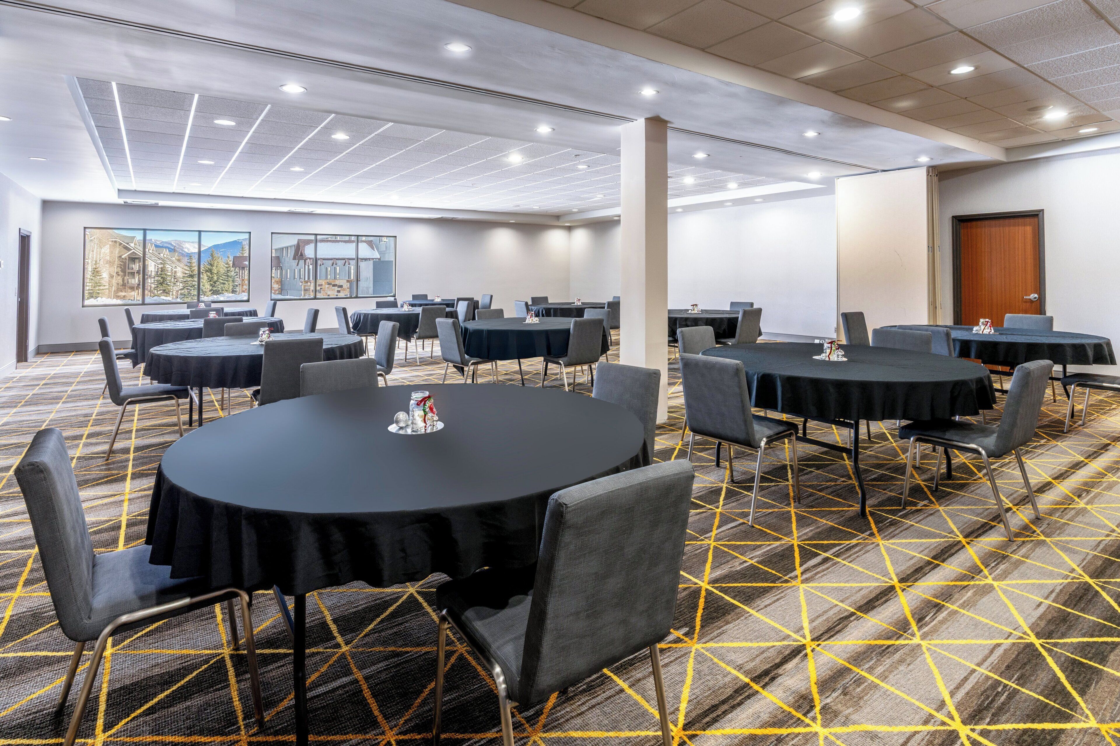 A conference room with multiple tables and chairs, carpeted floor, and large windows with a mountain view.
