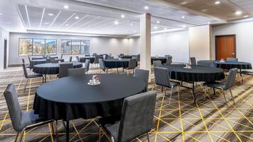 A conference room with multiple tables and chairs, carpeted floor, and large windows with a mountain view.