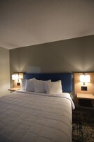 Habitación de hotel con una cama grande, dos mesitas de noche con lámparas, un cabecero azul y una alfombra estampada.