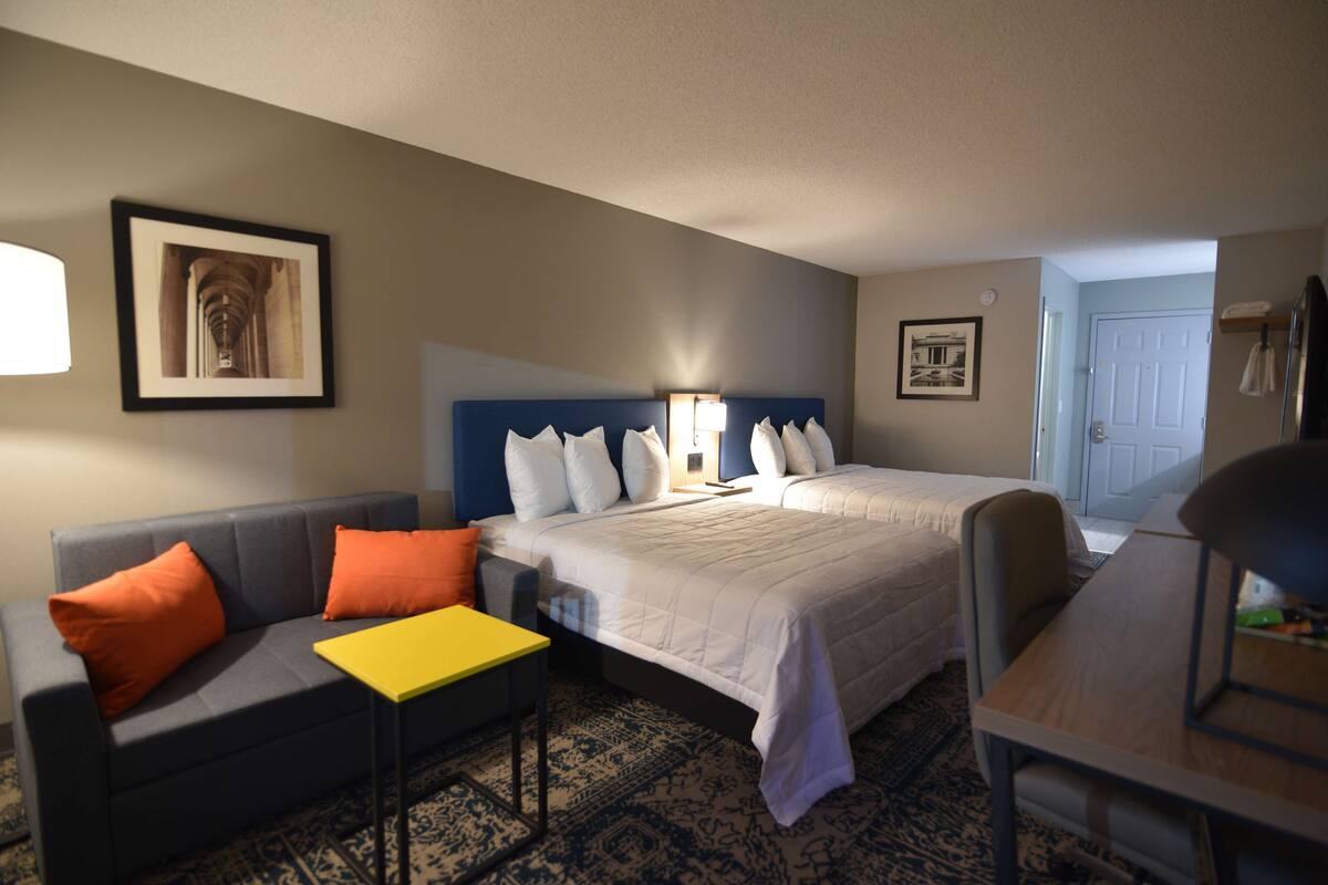 Hotelkamer met een bed, een bank, een klein tafeltje en een stoel. Twee ingelijste foto's hangen aan de muur.