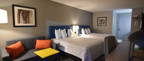 A hotel room with a bed, a sofa, a small table, and a chair. There are two framed pictures on the wall.