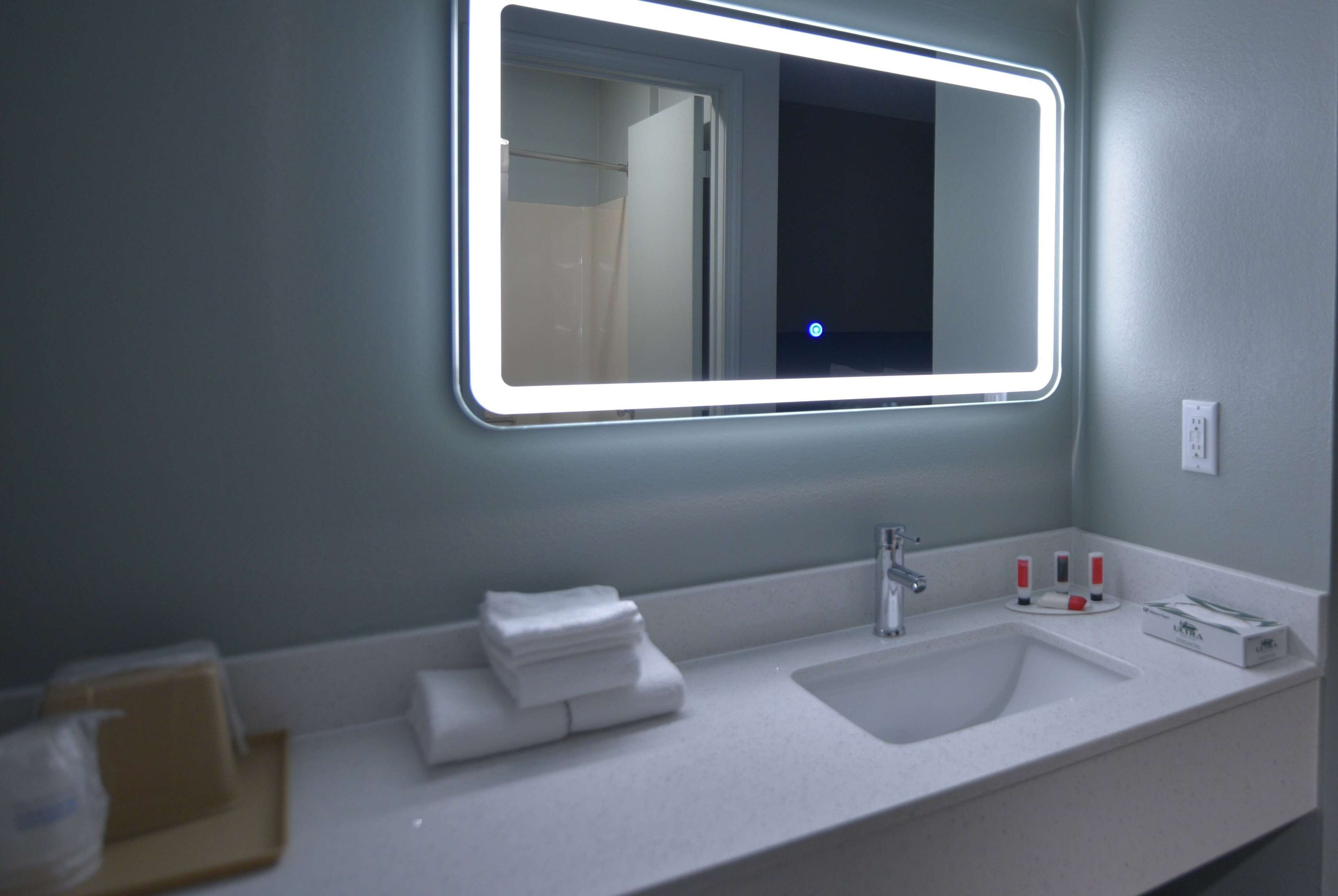 Een badkamer met een witte wasbak, een spiegel met verlichte randen en een handdoekhouder.