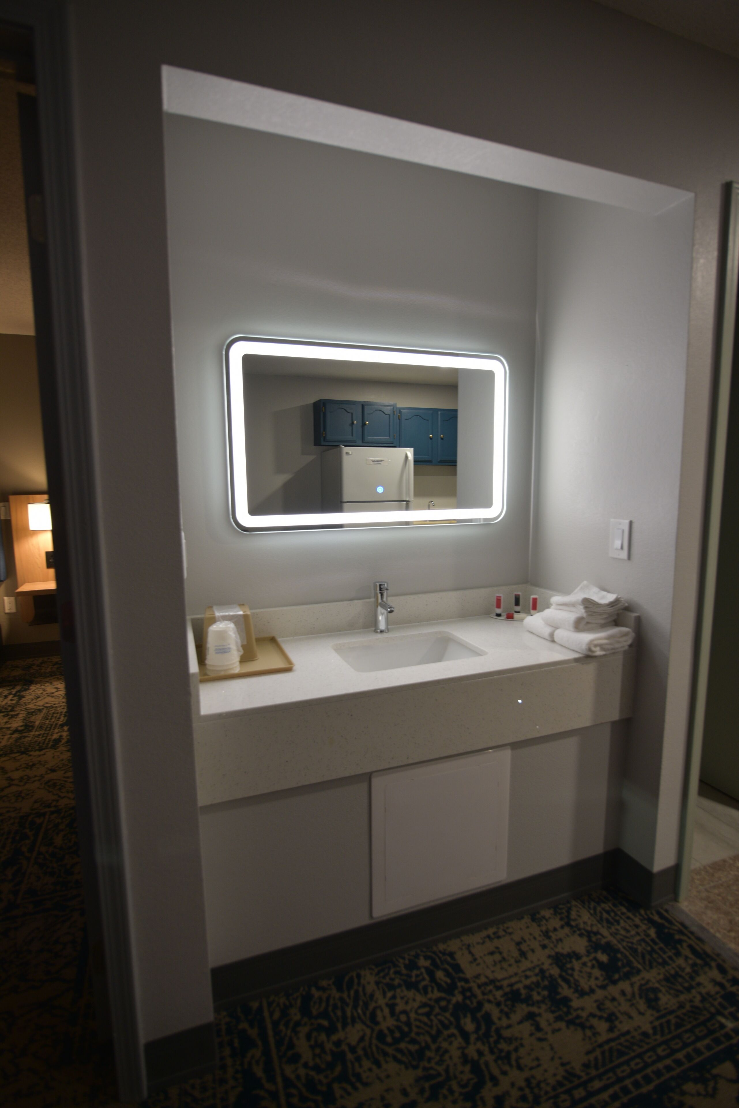 A modern bathroom with a large mirror, white sink, and a towel rack.