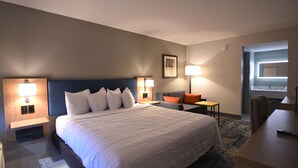 Une chambre d’hôtel avec un grand lit, deux tables de chevet avec des lampes, une petite table avec une chaise et un bureau avec une chaise.