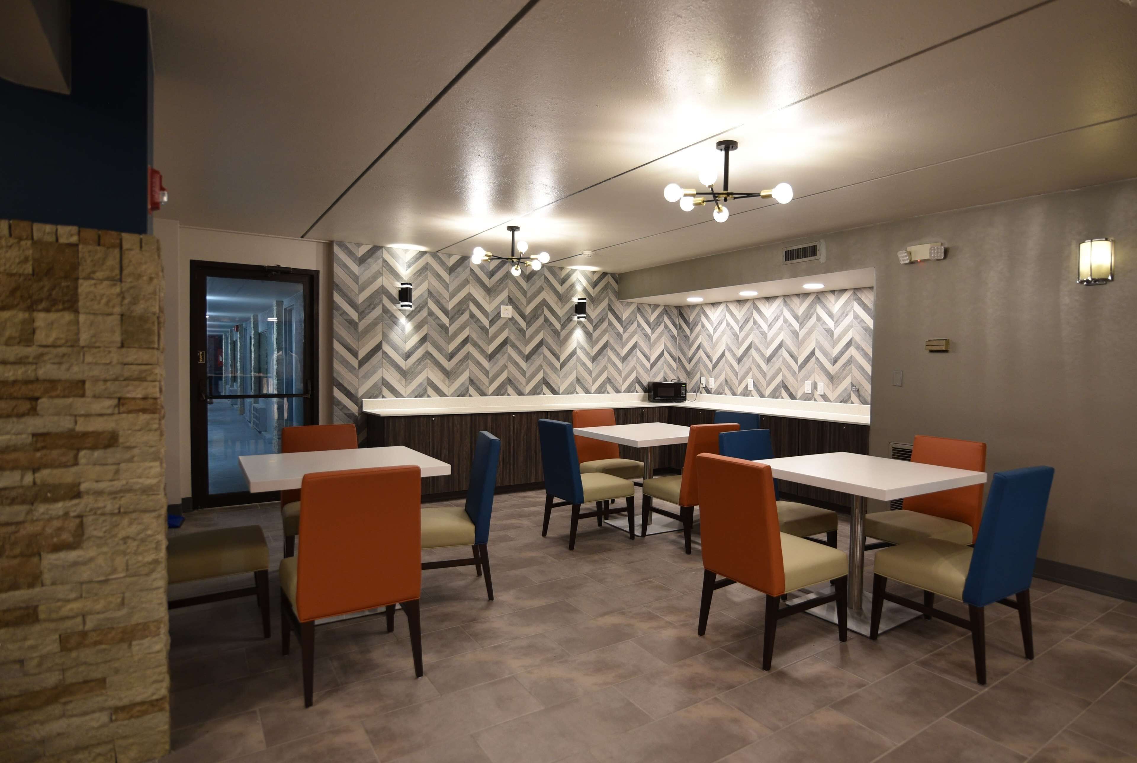 A modern dining area with a herringbone-patterned wall, a kitchen counter, and multiple tables and chairs.