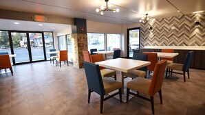 Un restaurant avec des tables et des chaises, un mur orné d’un motif en chevrons et une vue sur le parking, visible à travers de grandes fenêtres.