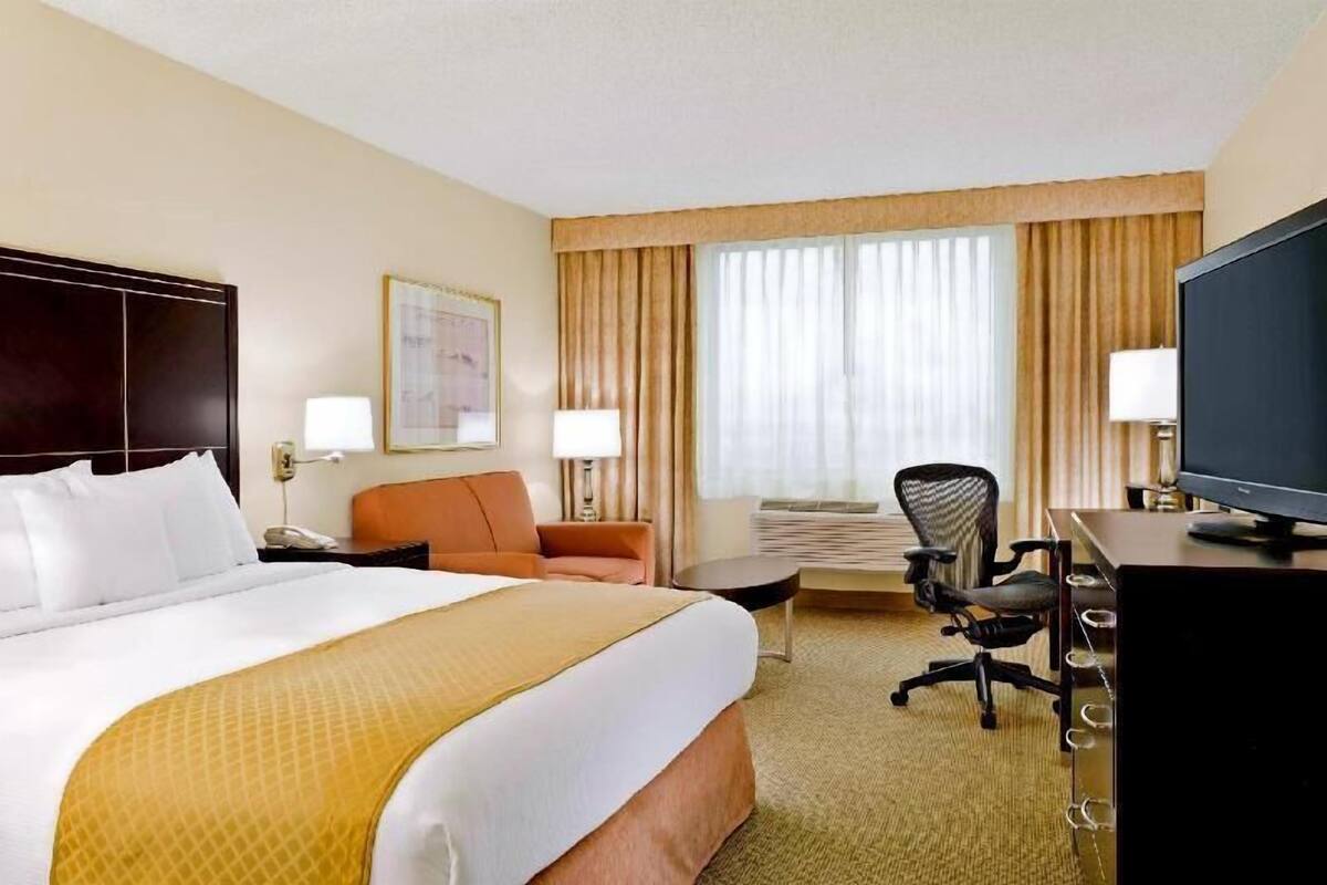 A hotel room with a large bed, a desk, a chair, a television, and a window with curtains.