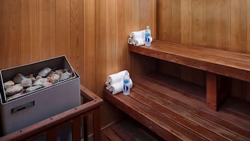 Una sauna con bancos de madera, una cesta de piedras y toallas.