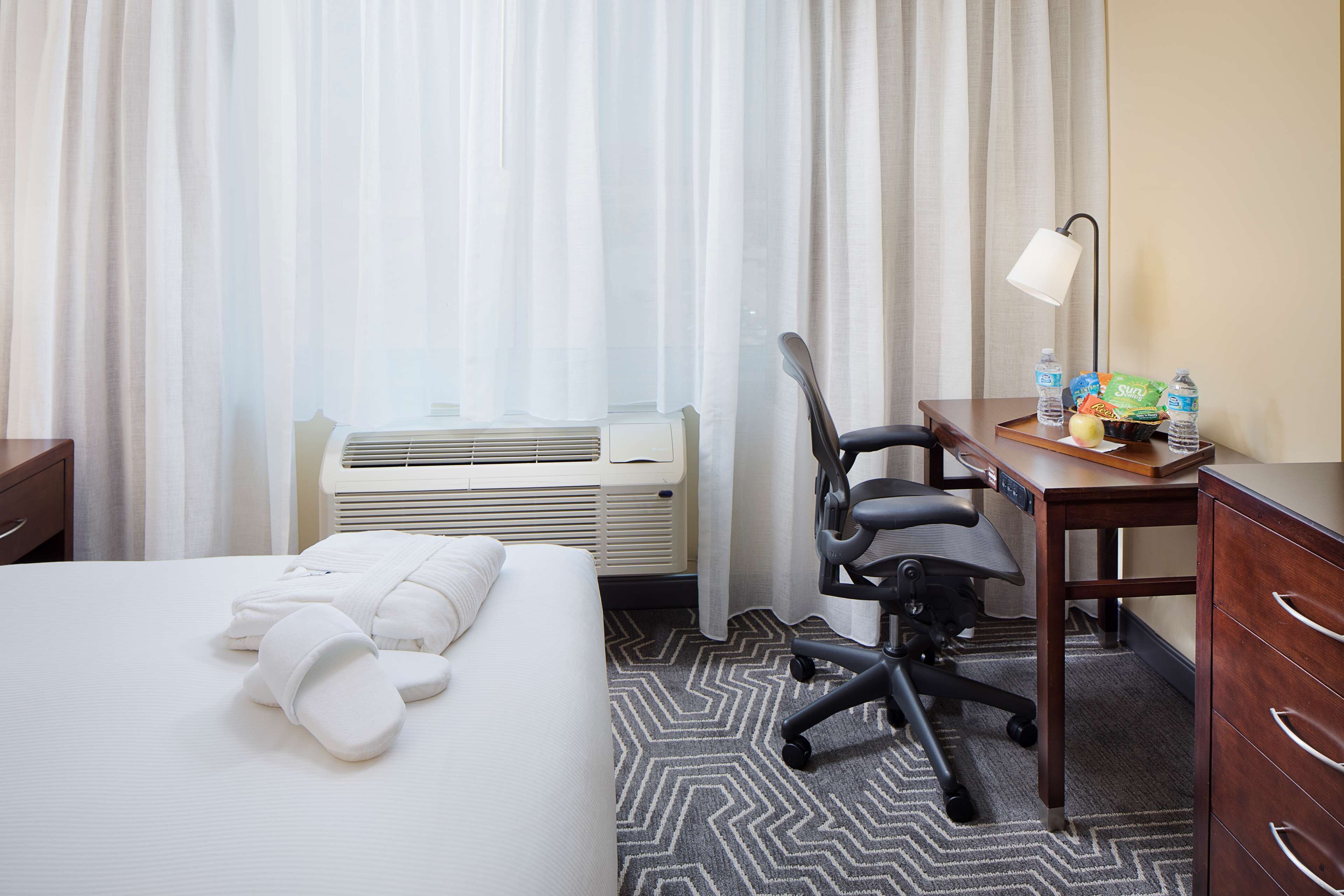 Una habitación de hotel con cama, escritorio, silla, lámpara y radiador.