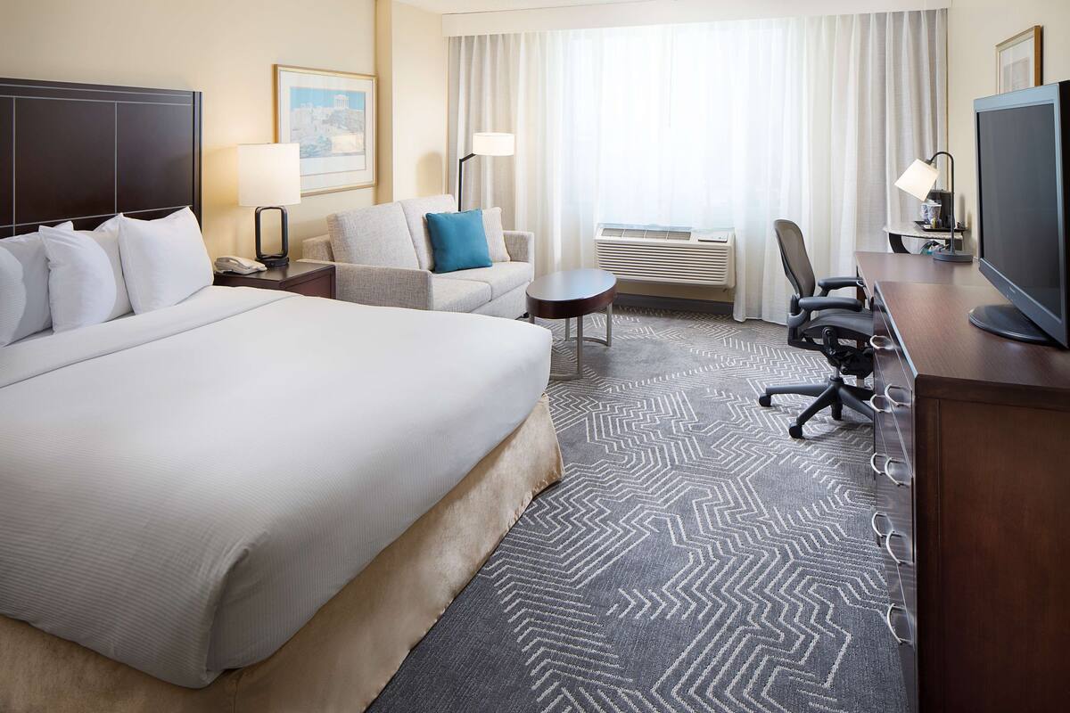 A hotel room with a large bed, a sofa, a desk, and a television.