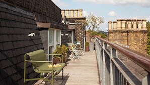 Una terraza en la azotea con cubierta de madera, un banco de metal y barandilla.