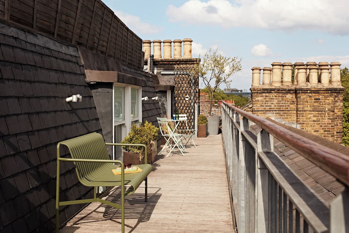A rooftop terrace with a wooden deck, a metal bench, and a railing.