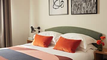 A neatly made bed with two orange pillows, a green headboard, and a bedside table with a lamp and a vase of flowers.