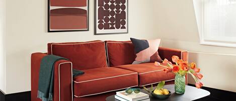 A modern living room with a red sofa, two framed abstract artworks, a coffee table with a book, glasses, and a vase with flowers.