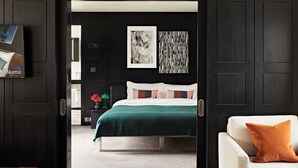 Un dormitorio moderno con una cama, una mesita de noche, una silla y una pared decorada con obras de arte.
