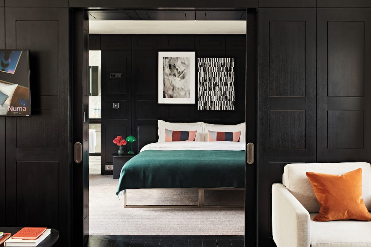 A modern bedroom with a bed, a nightstand, a chair, and a wall with artwork.