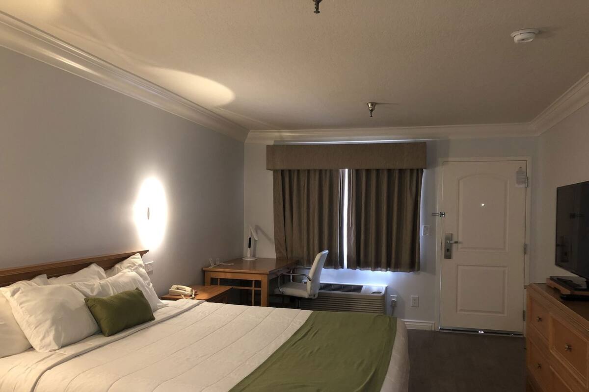 A hotel room with a bed, a desk, a chair, an air conditioning unit, a television, and a wardrobe.