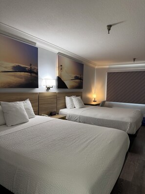 A hotel room with two beds, a nightstand, a lamp, and a painting of a bridge. - Days Inn by Wyndham Near City Of Hope (Duarte)