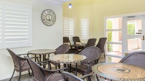 A sunlit room with wicker furniture, a round table with mosaic tiles, and a wall clock.
