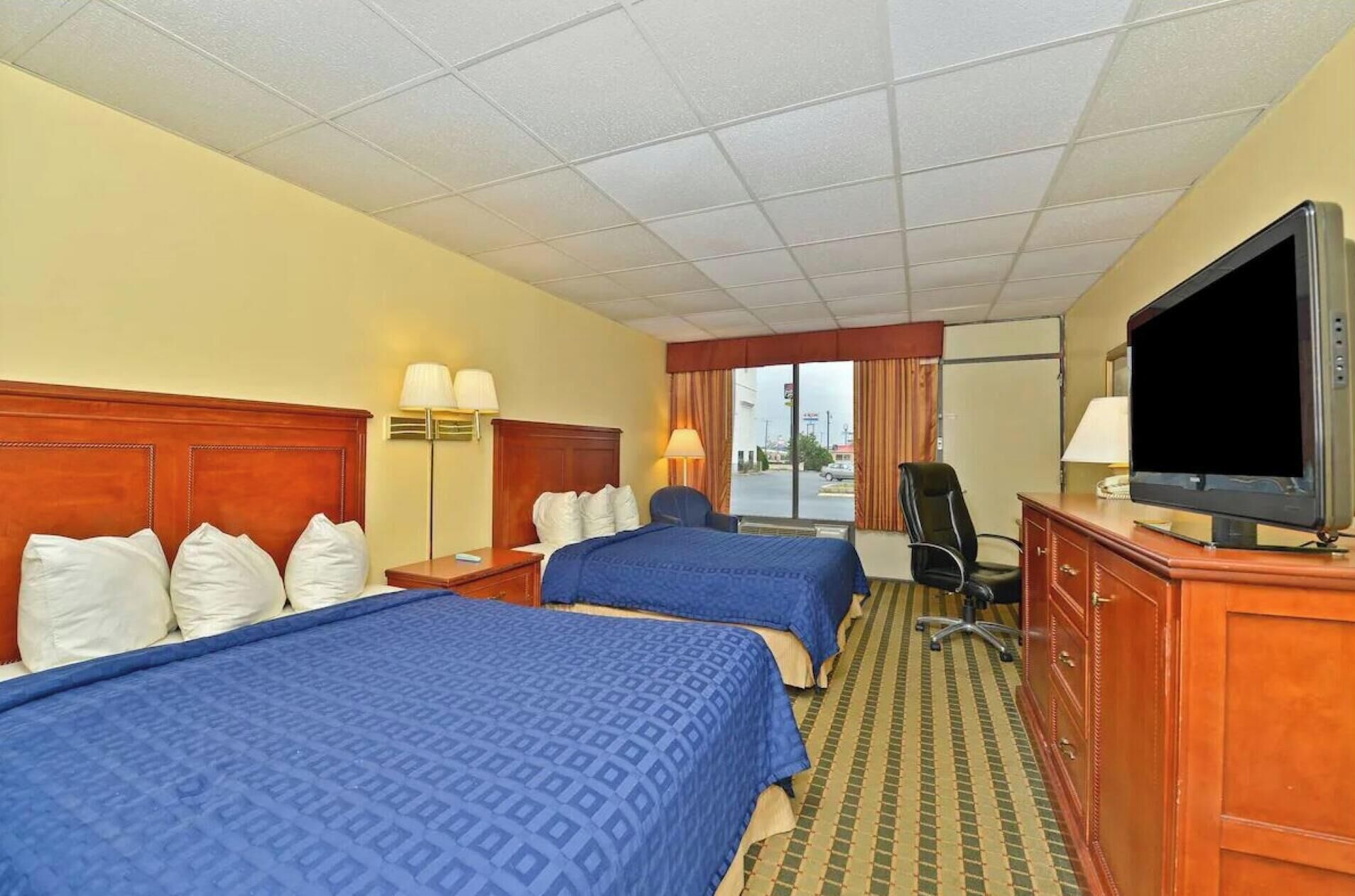 A hotel room with two beds, a television, a desk, and a chair.