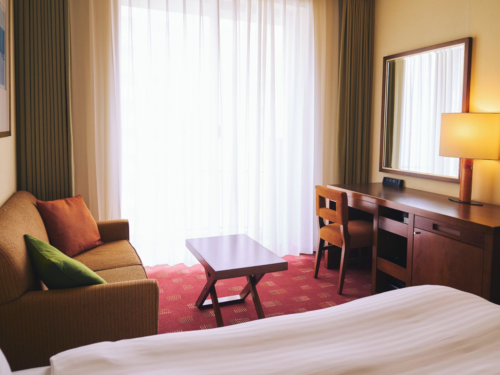 Une chambre d’hôtel avec un lit, un bureau, une chaise et une grande fenêtre avec des rideaux.