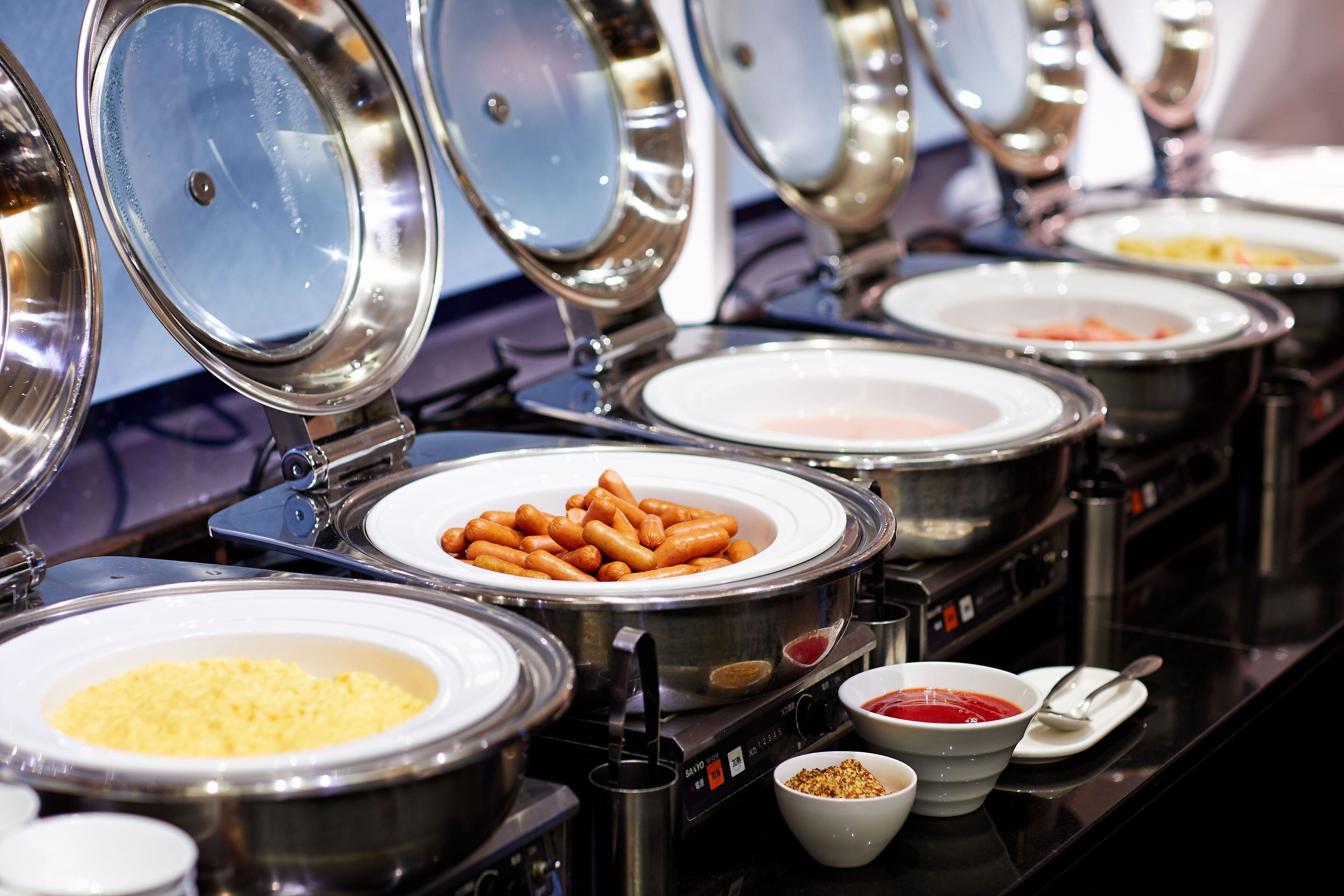 Un bufé con diversos alimentos, incluyendo salchichas, arroz y salsas.