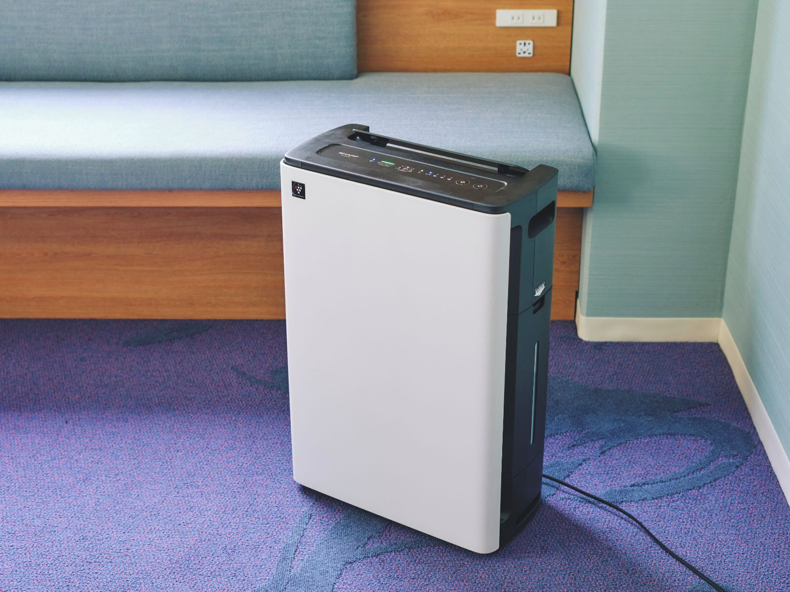 A compact, white and black portable heater in a room with a blue carpet and a wooden bench.
