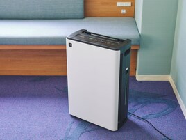 A compact, white and black portable heater in a room with a blue carpet and a wooden bench.