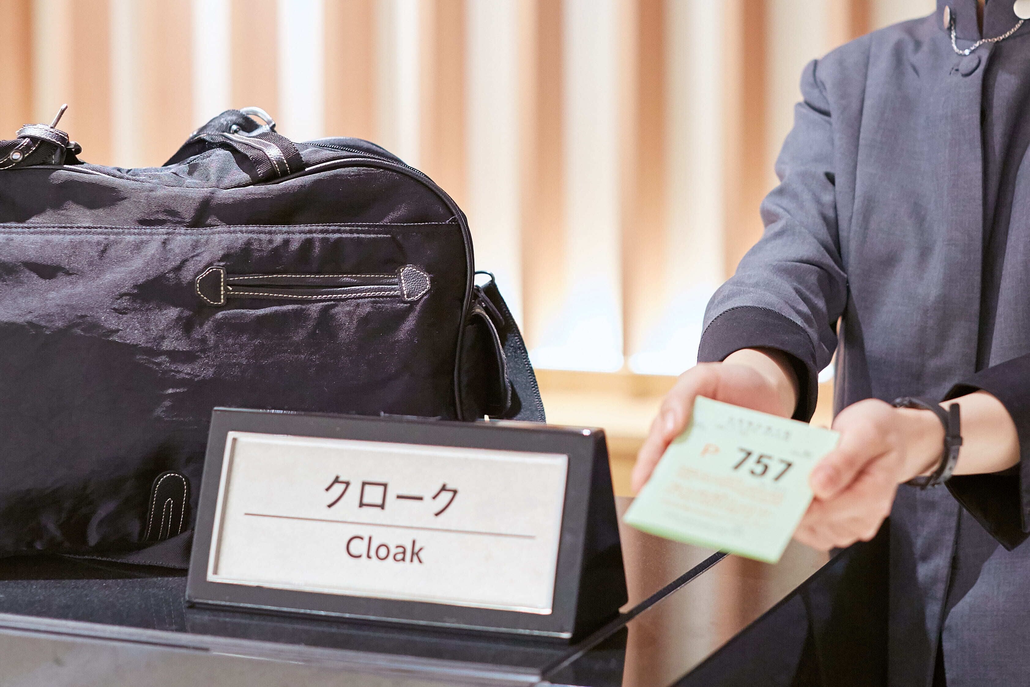 A black suitcase labeled "Cloak" and a person holding a card with the number "757".