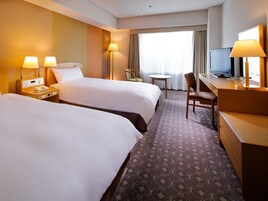A hotel room with two beds, a desk, a chair, a television, and a window with curtains.