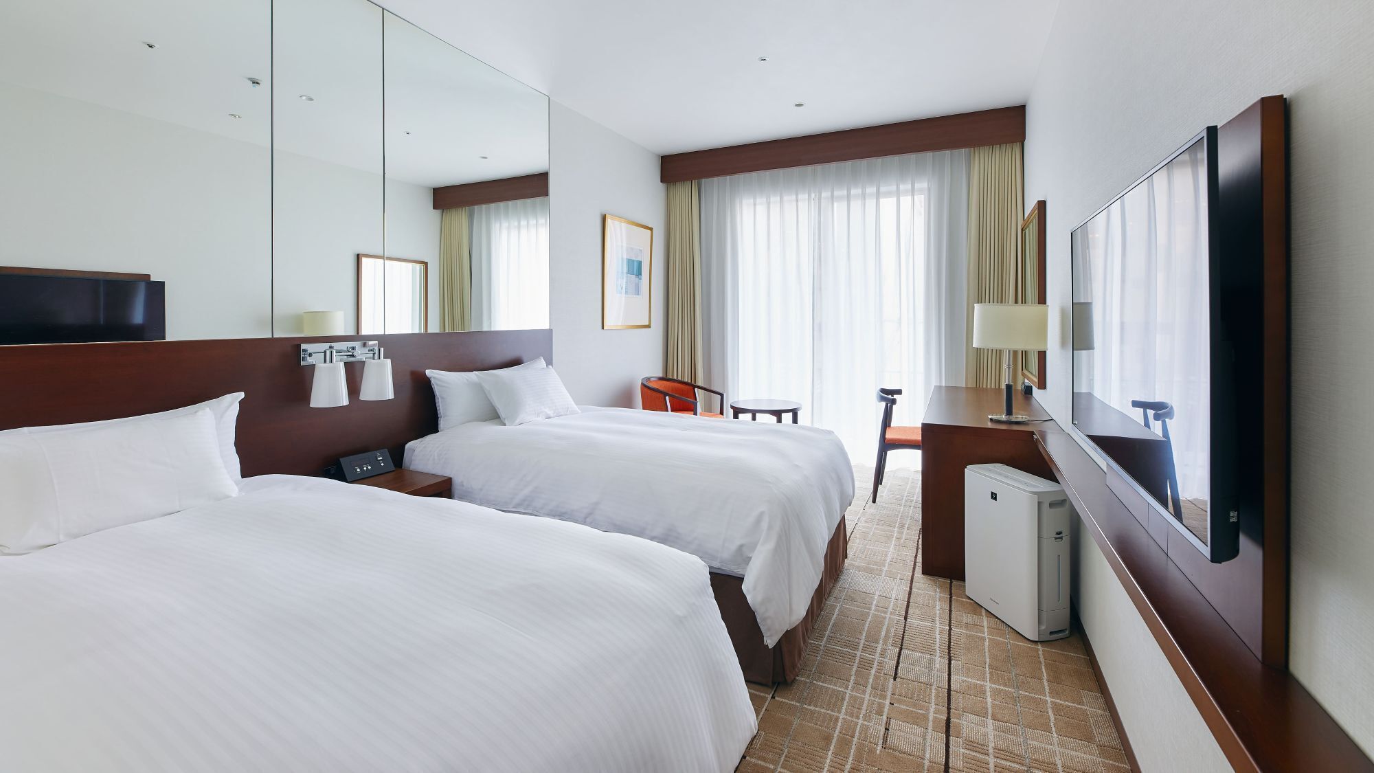 Quarto de hotel com duas camas, uma mesa, uma cadeira, televisão e minibar.
