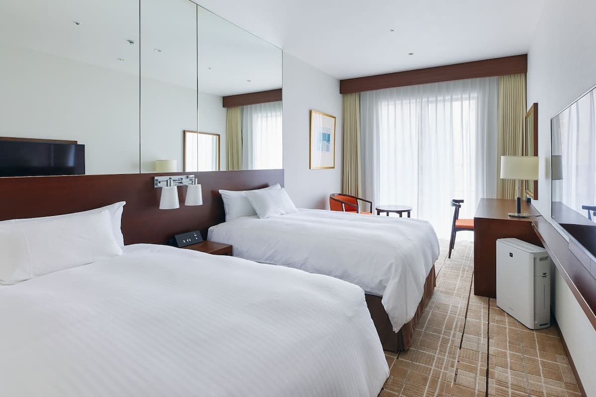 A hotel room with two beds, a desk, a chair, a TV, and a minibar.
