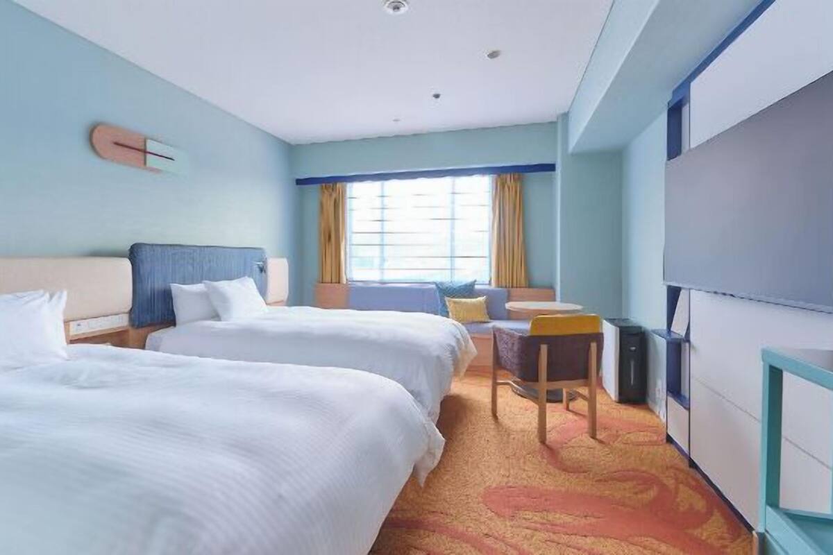 Une chambre d’hôtel avec deux lits, un bureau, une chaise, une télévision et une fenêtre avec des rideaux.