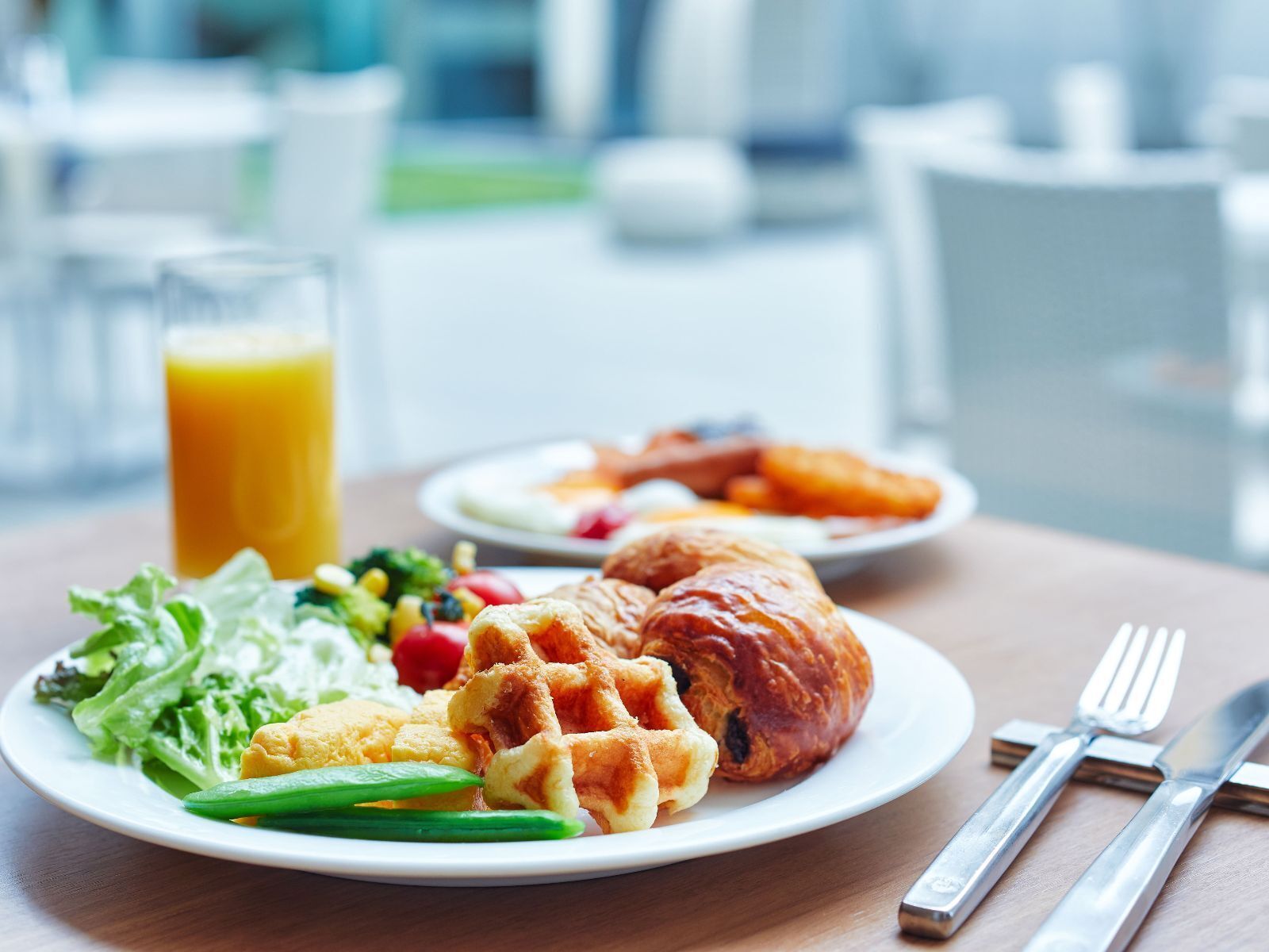 A breakfast setting with a plate of waffles, croissants, and a salad, along with a glass of orange juice.