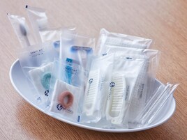 Divers articles de toilette, présentés dans des sachets en plastique transparent, sont disposés sur une assiette blanche.