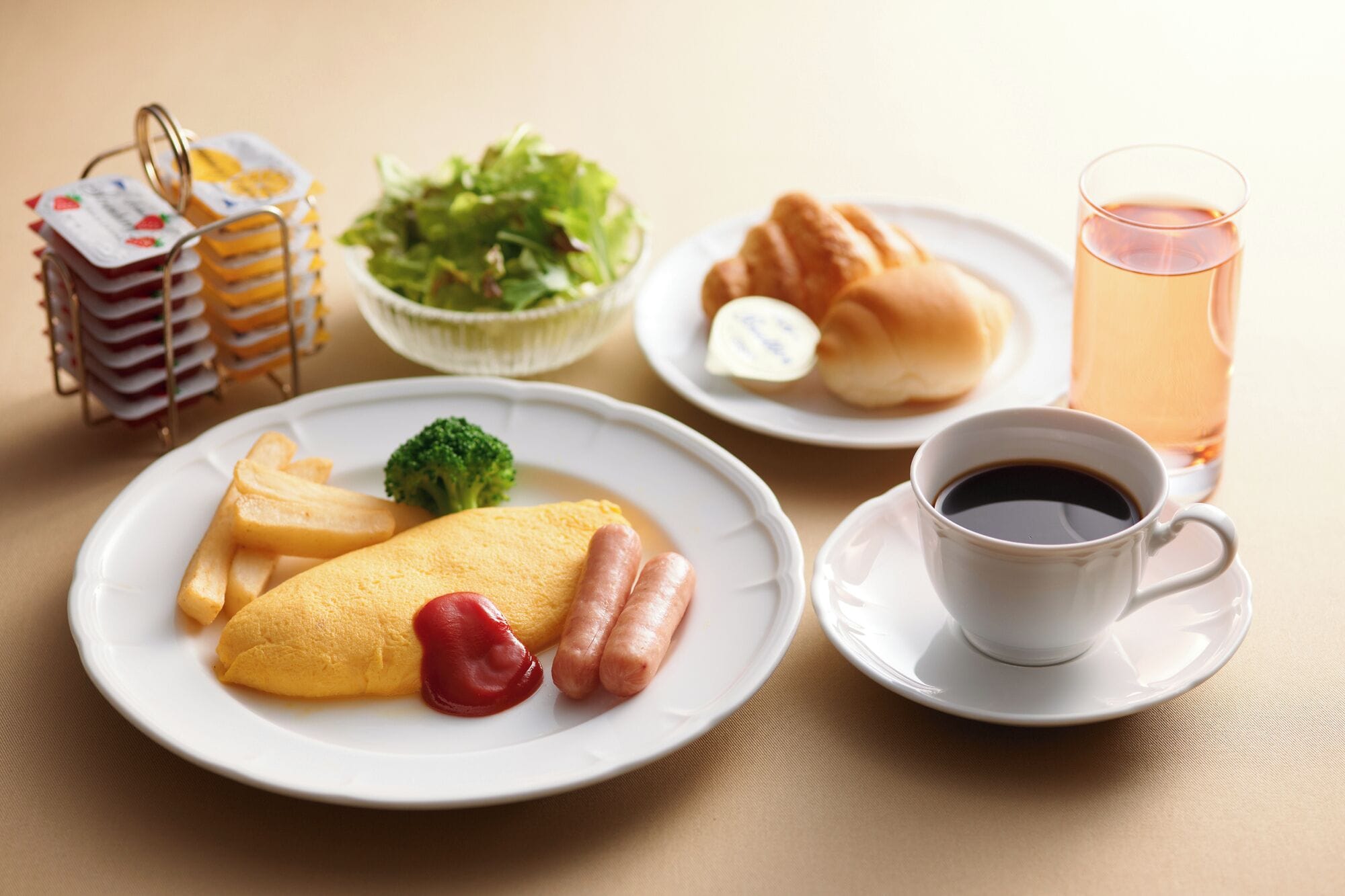 Une table dressée pour le petit-déjeuner, avec des assiettes remplies de nourriture, notamment des œufs, des saucisses et des frites, une tasse de café, un verre de thé et une salade.