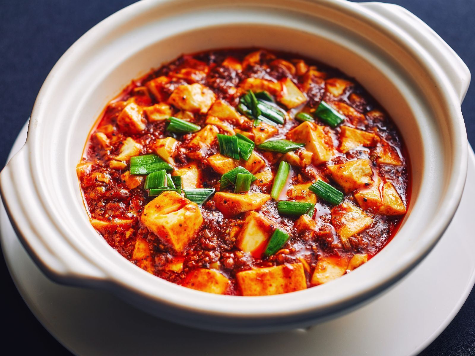 A bowl of spicy tofu dish garnished with green onions.