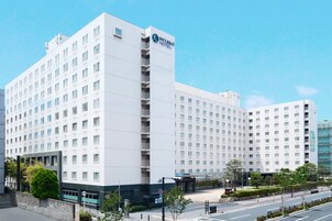 A modern hotel with a white facade, multiple balconies, and a clear blue sky.