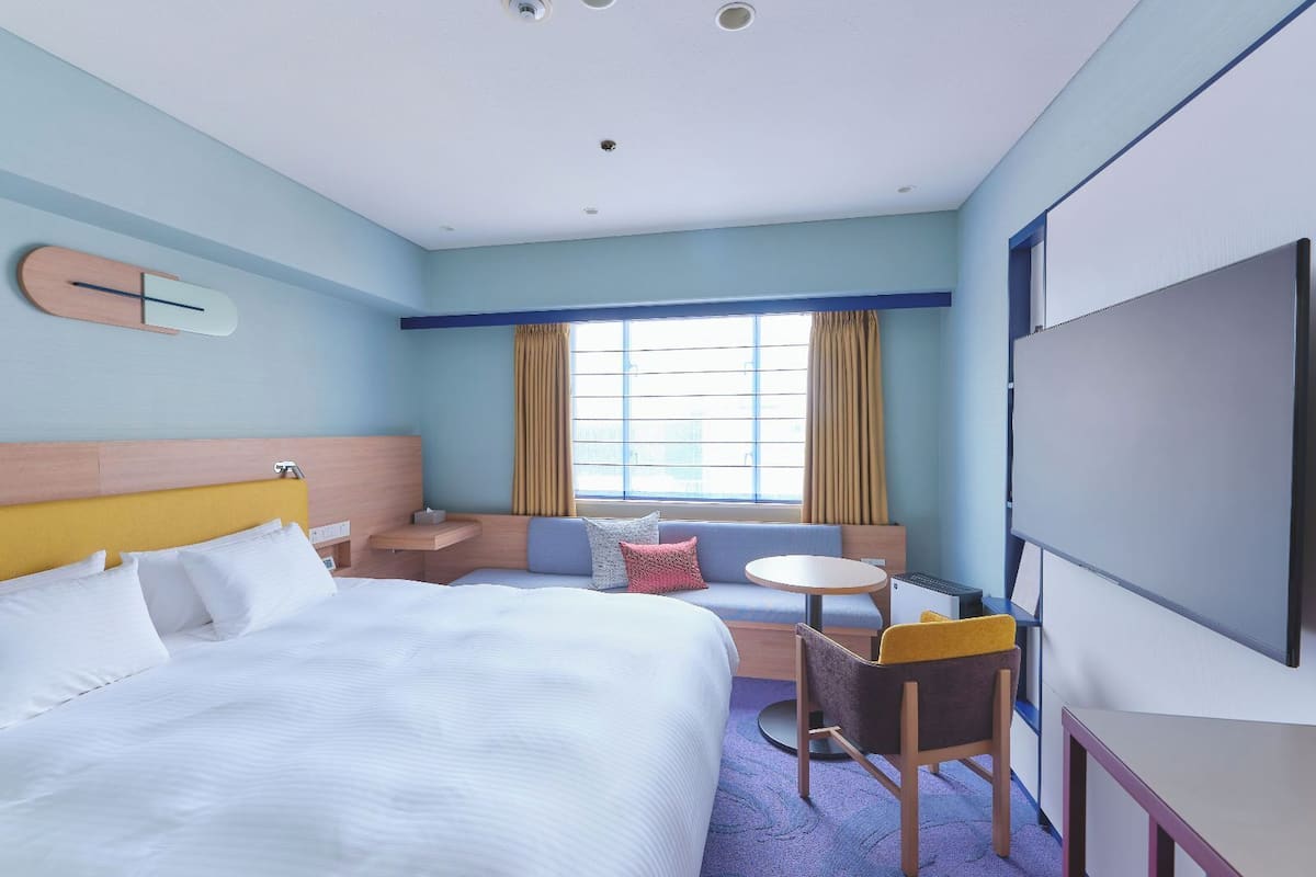 Une chambre d’hôtel avec un lit, un bureau, une chaise, une télévision et une fenêtre avec des rideaux.