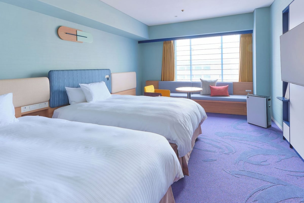 Une chambre d’hôtel avec deux lits, un canapé, une petite table et un téléviseur.