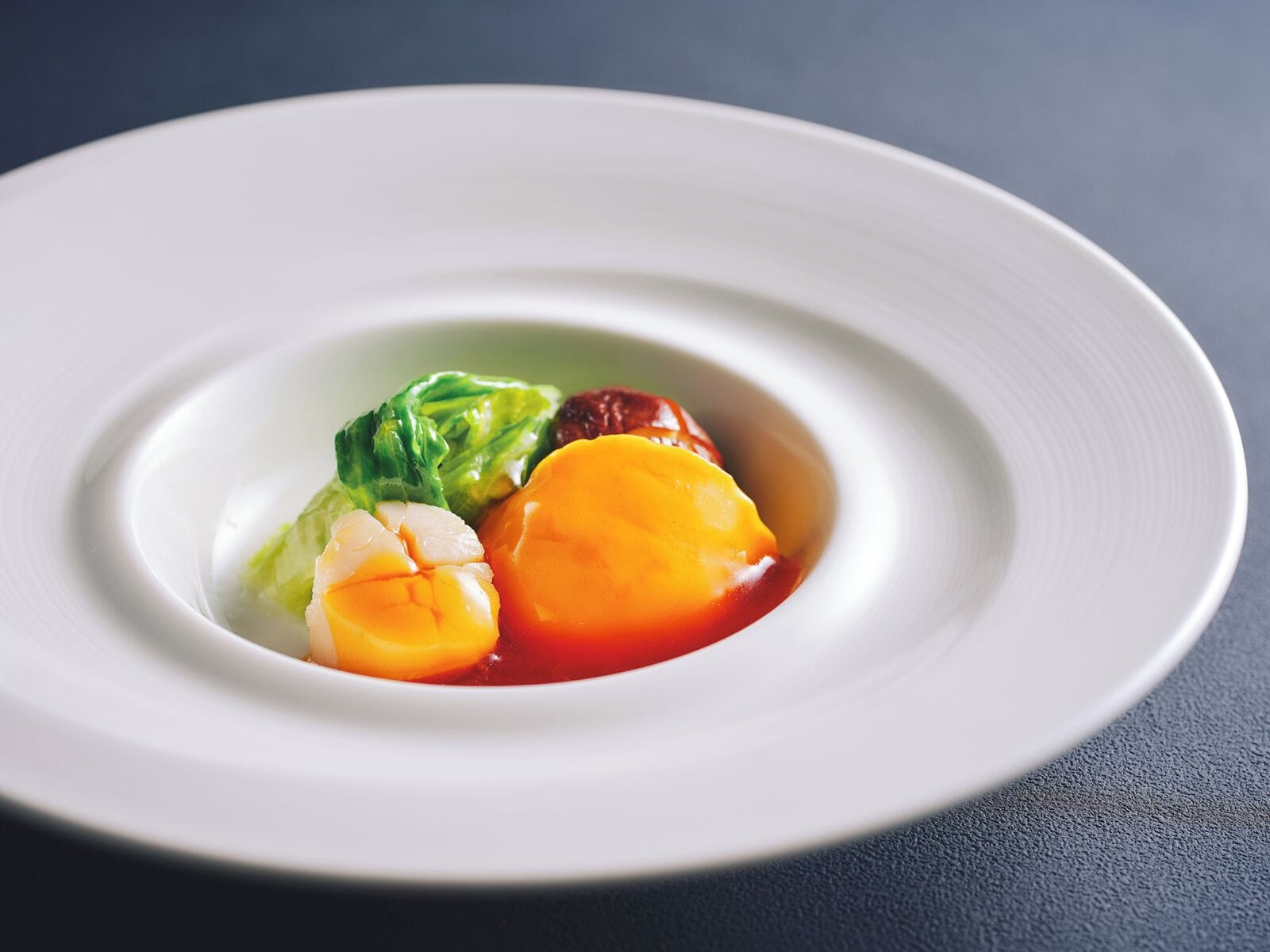 A white plate with a central arrangement of food items, including a piece of meat, a vegetable, and a fruit.