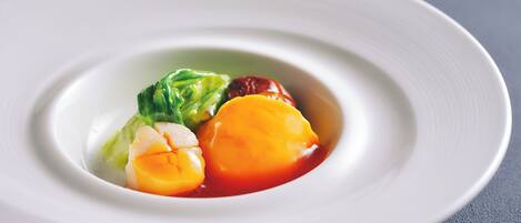 A white plate with a central arrangement of food items, including a piece of meat, a vegetable, and a fruit.