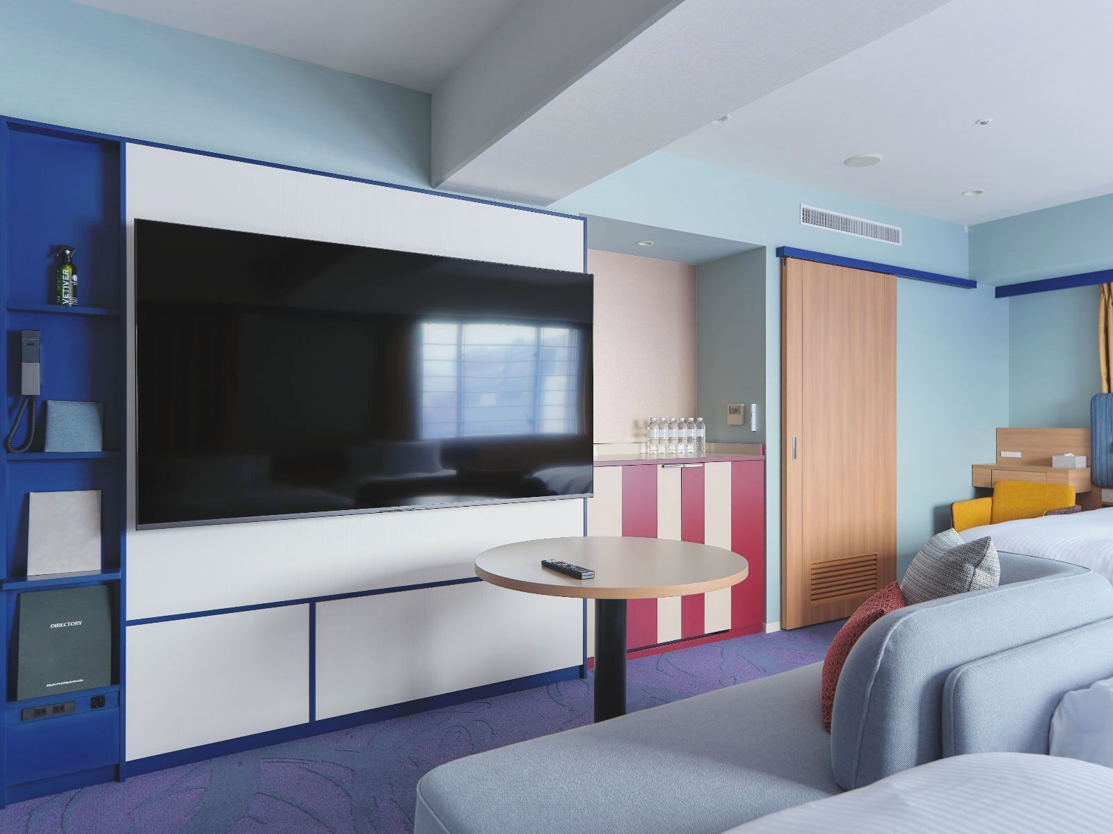 A modern hotel room with a large flat-screen TV, a small round table, a sofa, and a wardrobe.
