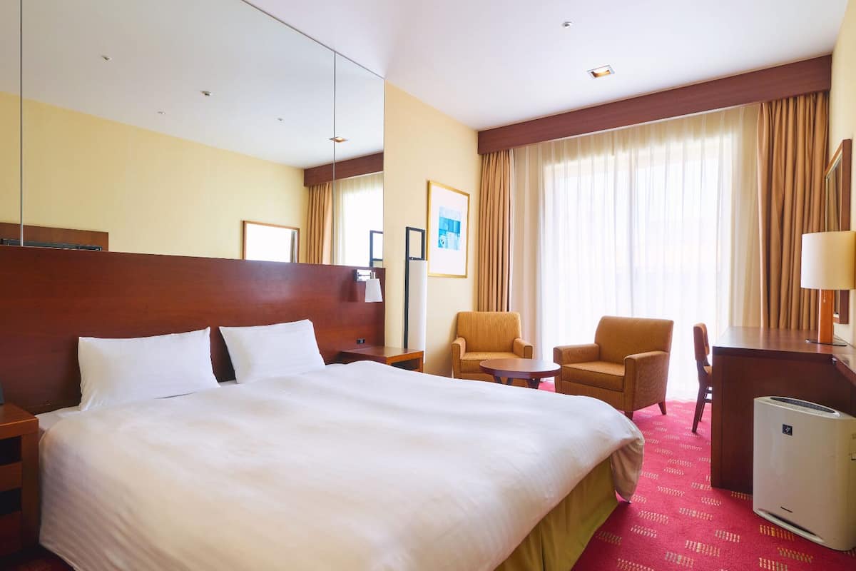 Une chambre d’hôtel avec un grand lit, deux fauteuils, un bureau et un radiateur portatif.