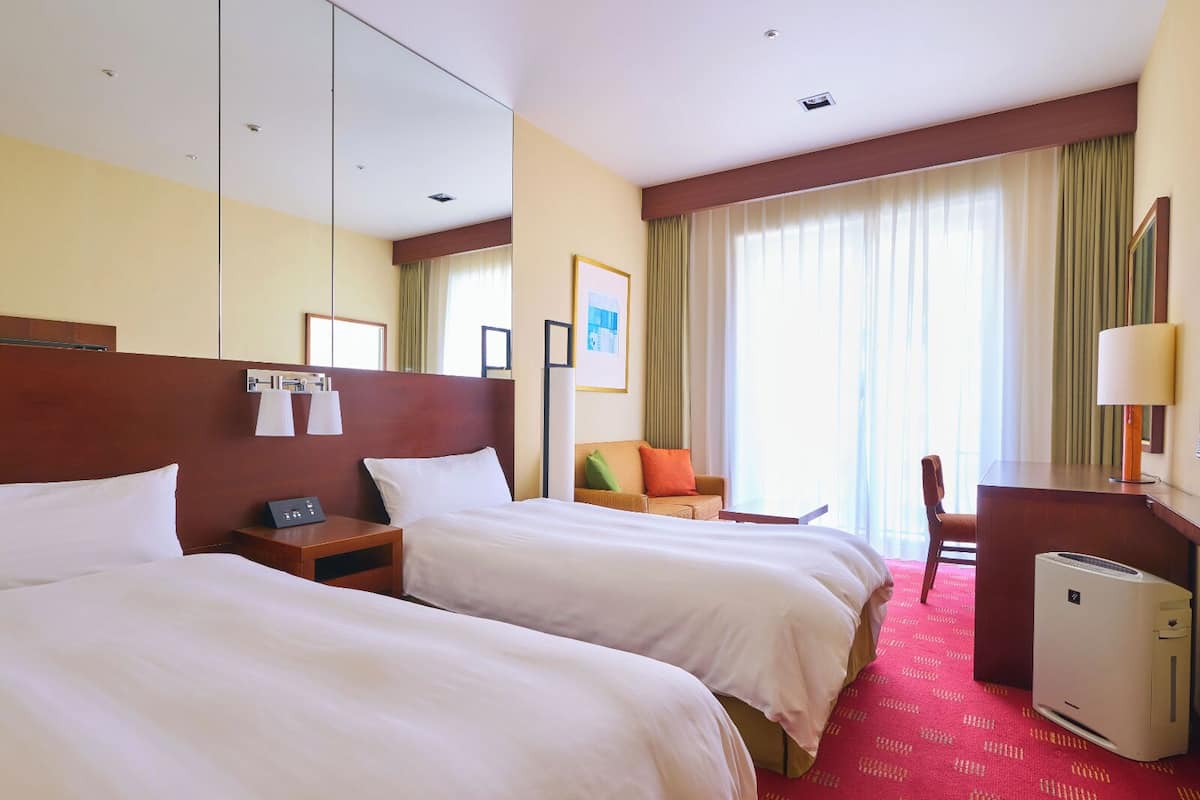 Une chambre d’hôtel avec deux lits, un bureau, une chaise, une lampe et un radiateur.
