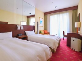 A hotel room with two beds, a desk, a chair, a lamp, and a heater.