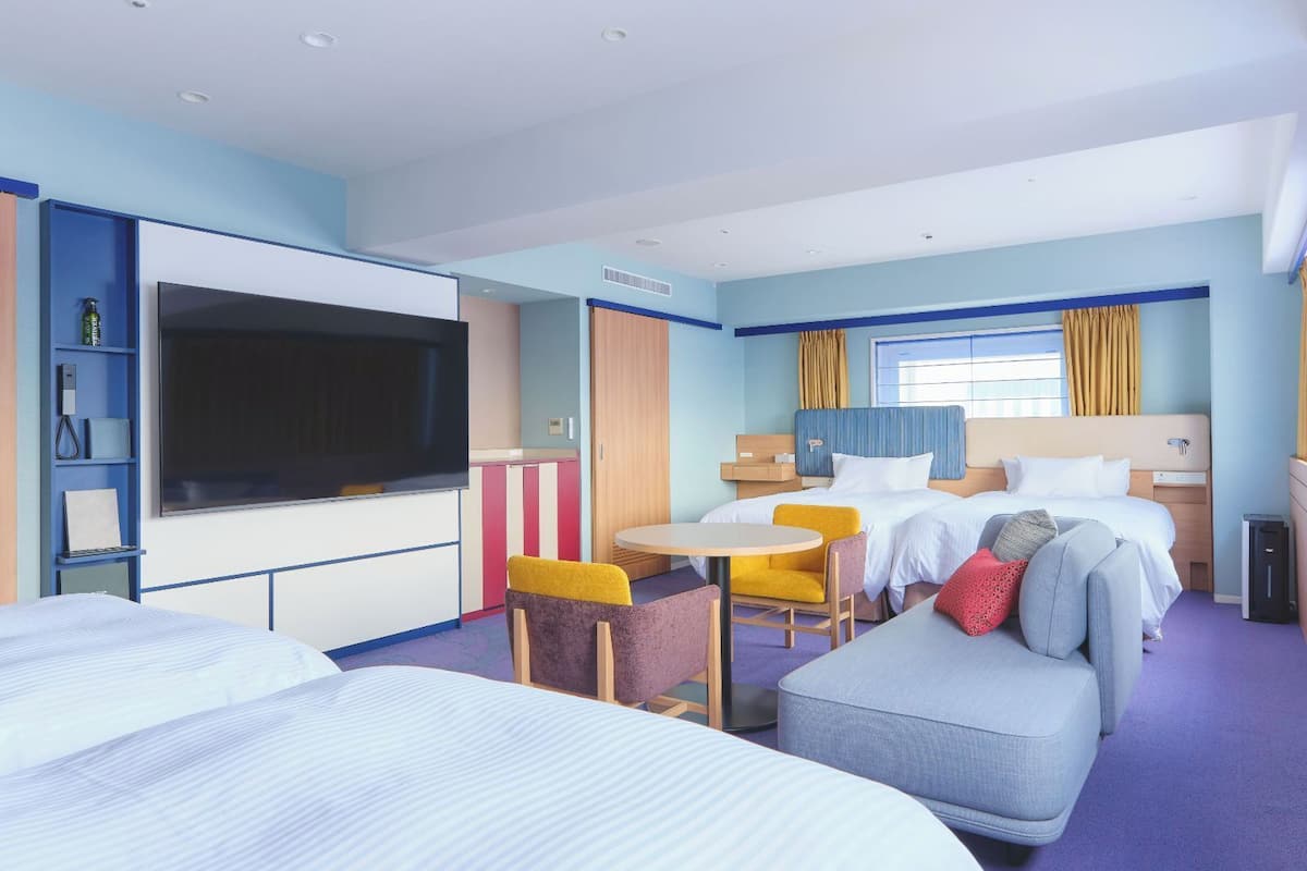 Une chambre d’hôtel avec deux lits, une télévision, une petite table et un canapé.
