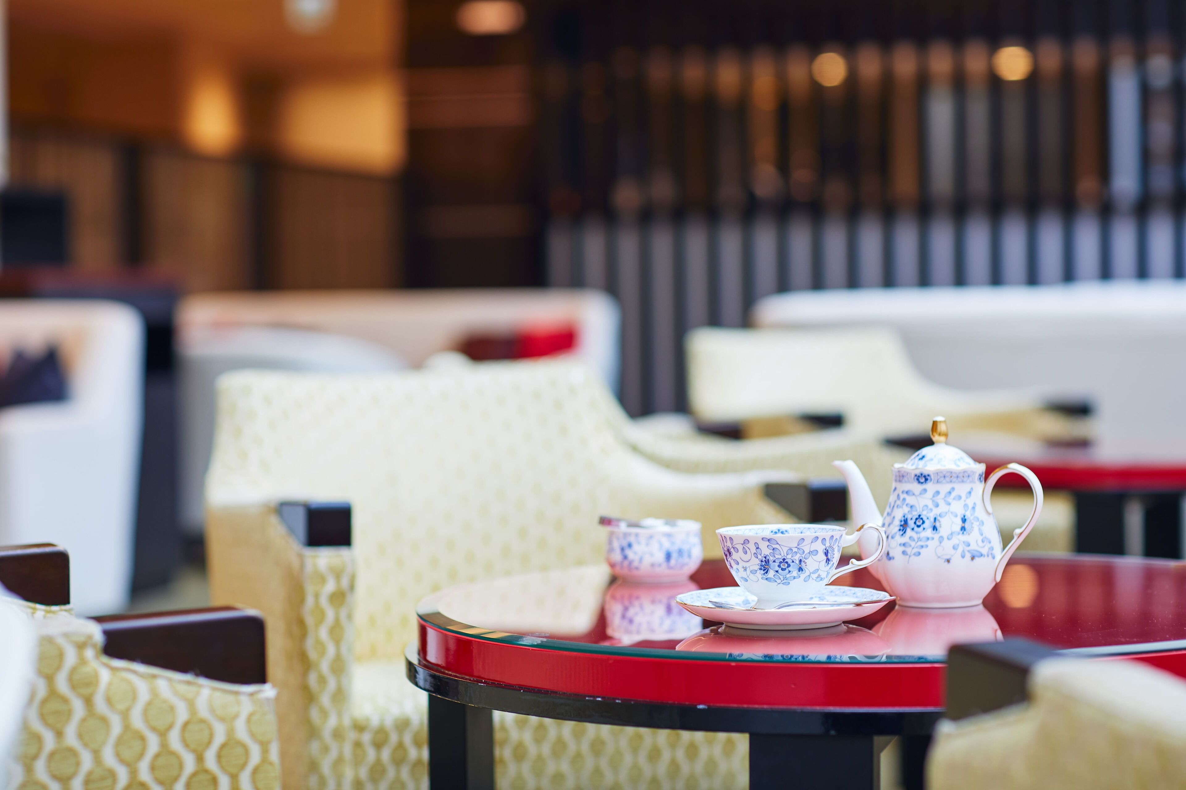 A table with a teapot and cups, surrounded by patterned chairs in a dining area.